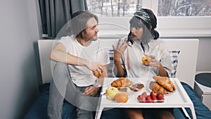 Lazy morning in bed. Young multiethnic couple drinking juice and having a breakfast in the hotel room on honeymoon