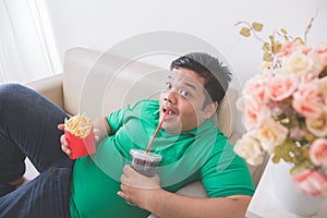 Lazy obese person eats junk food while laying on a couch