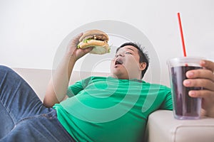 Lazy obese person eats junk food while laying on a couch