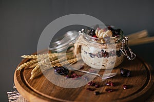 Lazy overnight oatmeal in glass jar with cherry and bananas on a dark black background on a wooden plate decorated with spikelets