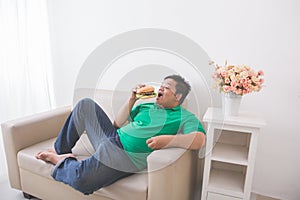 Lazy overweight man eating hamburger while laying on a couch