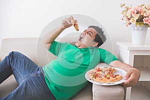 Lazy overweight man eating pizza while laying on a couch