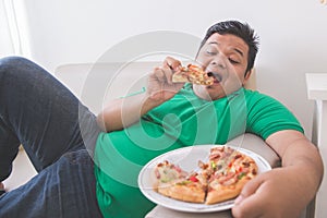 Lazy overweight man eating pizza while laying on a couch