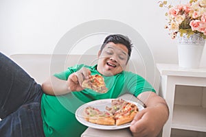 Lazy overweight man eating pizza while laying on a couch