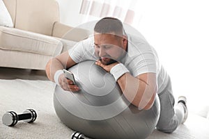 Lazy overweight man using smartphone while lying on exercise ball