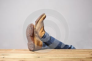 Lazy person concept: man`s legs wearing  blue jeans  of desert boots rest on a wooden table with copy space for your text