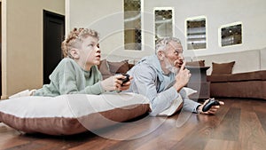 Lazy weekend with grandpa. Grandfather and his cute little grandson laying together on the floor and playing video games