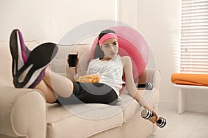 Lazy woman with sport equipment and junk food at home