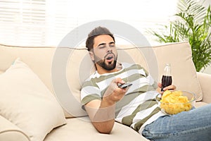 Lazy young man with chips and drink watching TV photo