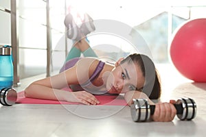 Lazy young woman with dumbbell lying on yoga mat indoors