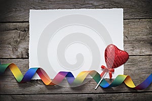 LBGTQ valentines day concept with rainbow ribbon and heart shape chocolate red lollipop on vintage wooden background