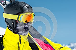 A lclose-up portrait of a skier in a protective helmet and glasses is a mask and scarf with skis on his shoulder in the