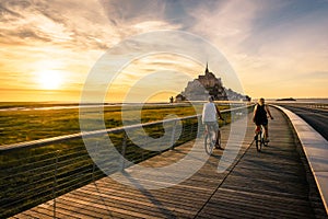 A couple of tourists biking at sunset towards the Mont Saint-Michel tidal island in Normandy, France