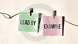 LEAD BY EXAMPLE, text words inscription on yellow sticker note on white wall or table