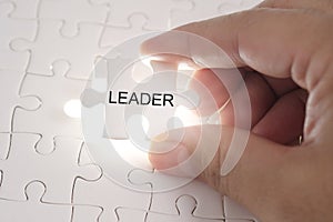 Leader word on jigsaw puzzle. Businessman hands holding white pu