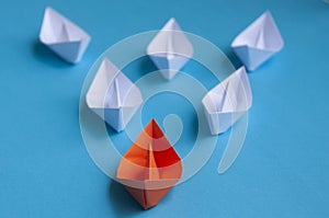 Leadership Concept - Orange color paper ship origami leading the rest of the white paper ship on blue cover background