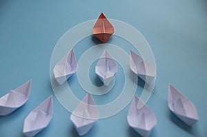 Leadership Concept - Orange color paper ship origami leading the rest of the white paper ship on blue cover background