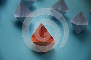 Leadership Concept - Orange color paper ship origami leading the rest of the white paper ship on blue cover background