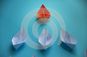 Leadership Concept - Orange color paper ship origami leading the rest of the white paper ship on blue cover background