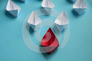 Leadership Concept - Red color paper ship origami leading the rest of the white paper ship on blue cover background