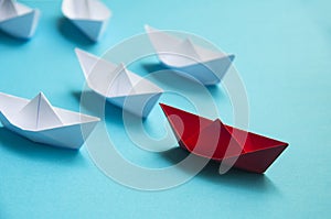 Leadership Concept - Red color paper ship origami leading the rest of the white paper ship on blue cover background