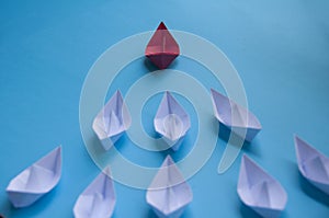 Leadership Concept - Red color paper ship origami leading the rest of the white paper ship on blue cover background