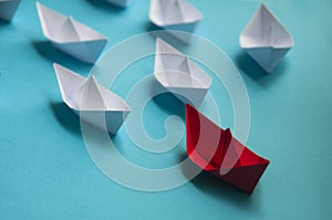 Leadership Concept - Red color paper ship origami leading the rest of the white paper ship on blue cover background