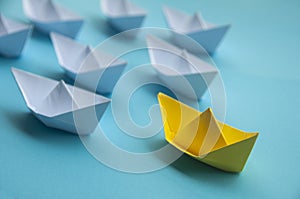 Leadership Concept - Yellow color paper ship origami leading the rest of the white paper ship on blue cover background