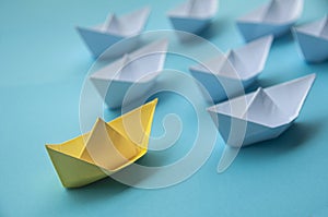 Leadership Concept - Yellow color paper ship origami leading the rest of the white paper ship on blue cover background