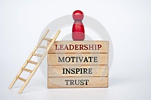 Leadership, motivate, inspire and trust text on wooden blocks with wooden red doll and ladder.