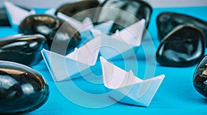 Leadership white paper boat lead further ships between abstract rock stones on blue background. Light Reflection in