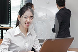 Leadership young Asian business woman looking at camera between listening to presentation in modern office background