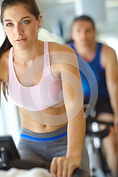 She leads a healthy lifestyle. A man and woman exercising in spinning class at the gym.