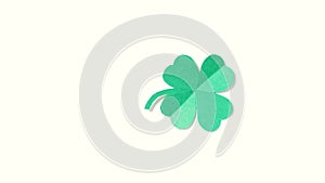 A leaf of clover cut out of paper is spinning on a shiny green background.