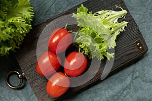 A leaf of fresh frieze lettuce and a branch with red ripe cherry tomatoes on a decorative kitchen board. Farm organic