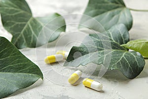 A leaf of ivy and pills on a light concrete table. Production of cough medicine with ivy extract. pharmaceutical industry