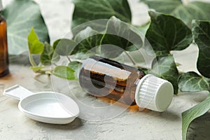 A leaf of ivy and syrup in a bottle on a light concrete table. Production of cough medicine with ivy extract. pharmaceutical indus