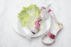 The leaf of lettuce on a white plate and measuring tape
