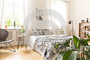 Leaf motif linen on a big bed in a modern bedroom interior with windows in a back wall. Real photo.