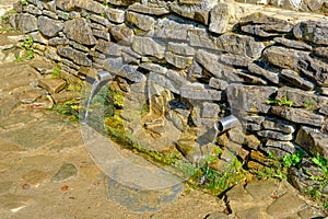 leakage of water from the ground through a metal pipe in two places with a stone wall. Healing springs in the Carpathians