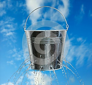 Leaky bucket with water against sky