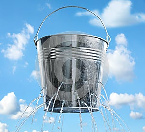 Leaky bucket with water against sky