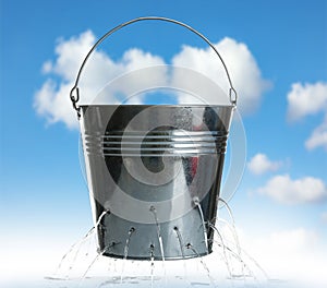 Leaky bucket with water against sky