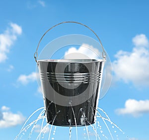 Leaky bucket with water against sky