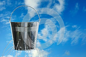 Leaky bucket with water against sky. Space for text