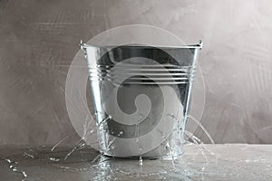 Leaky bucket with water on table against grey background photo