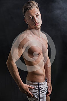 Lean athletic shirtless young man standing on dark background