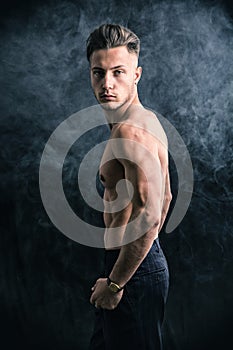 Lean athletic shirtless young man standing on dark background