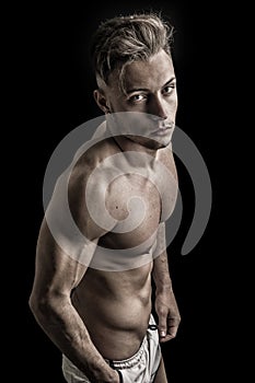 Lean athletic shirtless young man standing on dark background