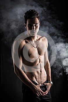 Lean athletic shirtless young man standing on dark background